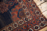 Antique Persian Afshar rug corner with dark blue field wear, terracotta floral border, tattered end.