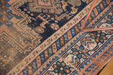 Antique Afshar rug close-up: navy field, stepped geometric motifs, time-softened apricot, sky blue.