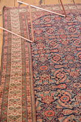 Angled view of the germinating plant border alongside the navy Herati field of an antique Mission Malayer rug.