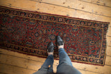 Feet on vintage Lilihan runner, showing dense floral bouquets, low pile, and tattered edges.