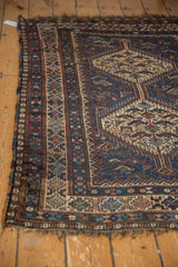 Vintage Qashqai rug corner showing geometric hook-and-latch border motifs, navy blue, and tattered fringe.