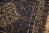 Vintage Qashqai rug corner with geometric borders, stylized forms on navy, and tattered fringe.