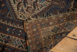 Folded corner of a vintage Qashqai rug, showing geometric pattern, foundation, and fringed edge.