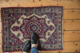 A small antique Kermanshah rug with a red and blue medallion, shown for scale underfoot.