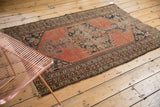 Faded brick red field, dark navy herati spandrel, floral borders, and subtle wear.