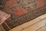 Malayer rug's main border showing pinwheel florals, meandering vines, and a faded brick red field.