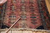 Textured antique Lilihan rug fragment showcasing faded raspberry plant motifs and tattered fringe.