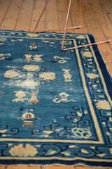 Antique Chinese Peking rug section with denim blue field, ivory floral motifs, urns, and central wear.