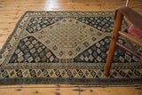 Aged corner of an antique Shirvan rug, detailing geometric starburst patterns in navy, sand, and sky blue.