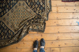 Partially unrolled antique Shirvan rug displaying navy blue and sand geometric patterns.