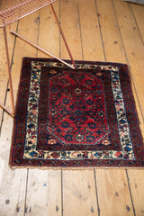 Angled view of a vintage Engelas square rug showing its red Herati field and ivory vine border.