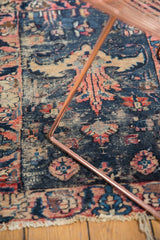 Close-up of antique Lilihan rug's end with tattered fringe and rose, navy motifs.