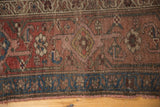 Tattered edge of an antique Kurdish Bijar rug, showing blue geometric border and blush floral motifs.