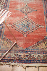 Tattered fringe, faded blush red field, and navy blue border of an antique Malayer rug.