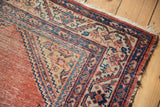 Antique Malayer rug corner, displaying coral field, navy border, ivory traditional patterns, and tattered fringe.