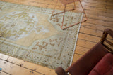 Distressed corner of a Vintage Oushak rug with beige, moss green arabesque spandrel and fringed edge.