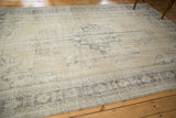 Distressed vintage Oushak rug corner detail, showing faded charcoal motifs on an open beige field.