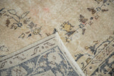 Distressed vintage Sivas carpet corner showing worn beige pile, subtle blush tones, and dark blue border reverse.