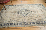 Distressed Sivas rug corner, charcoal blue scrolling border on beige field, with faint blush.