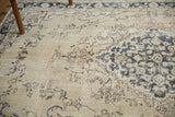 Distressed pile of Sivas carpet showing ornate scrolling vinery, beige, charcoal blue, faint blush.