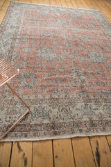 Distressed corner of a vintage Sparta carpet showing worn scrolling vinery in dusty rose, seafoam, and ivory.