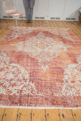 Distressed vintage Oushak rug corner: cherry red, tangerine field, ornate ivory pattern, and secure fringe.