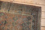 Distressed vintage Belouch rug corner with worn fringe, geometric border, and faded copper and sky blue.