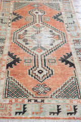 Distressed Oushak rug corner: cinnabar red field, seafoam green spandrel with plant motif, and fringe.
