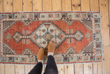Distressed vintage Oushak rug corner with pale brick red field and germinating plant motif.