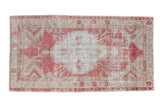 Distressed vintage Oushak rug with a faded raspberry red scalloped medallion on a beige field.