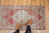 A top-down view of the distressed vintage Oushak rug's faded red and ivory pattern.