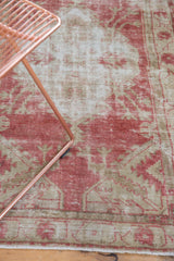 Distressed texture of the vintage Oushak rug showing faded raspberry red and beige motifs.