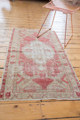 Vintage distressed Oushak rug in dusty raspberry and beige, styled in a room.