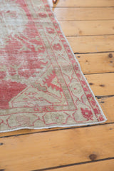 Corner view of a distressed Oushak rug showing the intact side selvage and even wear to the pile.