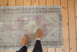 Worn vintage Oushak rug corner with distressed pile, mauve petals, and zig-zag border.