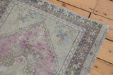 Corner of distressed Oushak rug, showing faded mauve, blue spandrels, and zig-zag border.