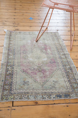 Distressed vintage Oushak rug corner, revealing pale aubergine and slate blue zig-zag border.