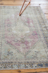 Distressed Oushak rug pile detail, featuring a zig-zag border and soft mauve and pale blue tones.