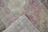 Vintage distressed Oushak rug corner revealing worn mauve pile and woven foundation with intact selvage.