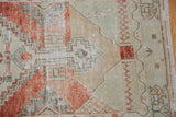 Distressed Oushak rug corner, with faded red, beige, seafoam green, and geometric spandrel motifs.