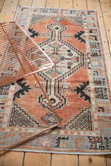 Distressed vintage Oushak runner's low pile, revealing faded cherry red and slate blue patterns.