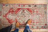 Distressed vintage Oushak rug with cherry red field, ivory corner spandrel, and primitive floral border.