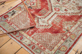 Distressed vintage Oushak rug corner showing cherry red abrashed border and ivory lattice spandrel.