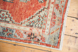Abrashed corner of a distressed vintage Oushak rug, showing primitive floral motifs in blush and seafoam.