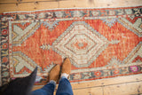 Distressed vintage Oushak corner, faded red field, pale green spandrel, charcoal border.