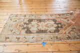 Overall view of distressed vintage Oushak runner with faded charcoal, terracotta, and splayed floral cross-sections.