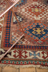 Antique Kazak rug's geometric border with madder red, navy blue, celadon, light pile, and fringe.