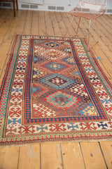 Bottom edge of antique Kazak rug with geometric motifs, fringe, and light pile.
