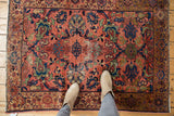 Feet on vintage Malayer rug, dusty blush rose field, navy blue motifs, low pile wear.