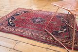 Corner of vintage Bijar rug with cherry red field, navy border, and geometric herati.